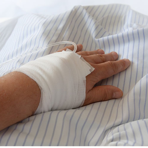 Eine Hand auf einer gestreiften Decke die Verbunden ist und aus dieser ein Infusionsschluach hervorgeht.jpg